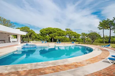 a large swimming pool with blue chairs and trees at Apartment Victoria - Quinta do Lago in Quinta do Lago