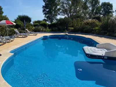 a blue swimming pool with chairs and an umbrella at Quinta Verde Albufeira in Albufeira
