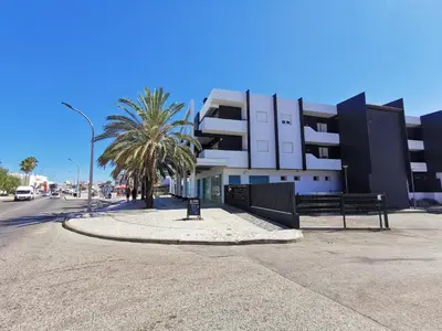 a building on a street with a bench and palm trees at AlbufeiraMar Beach Apartment in Albufeira