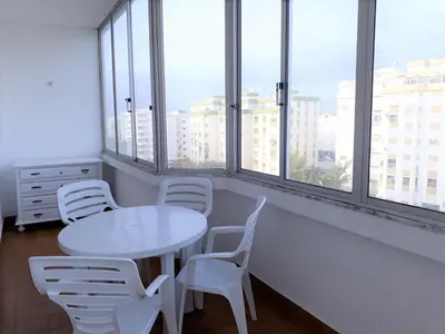 a white table and chairs in a room with windows at Torre 6- Vista Cidade, Aconchegante, 80mt Praia, Wifi in Quarteira