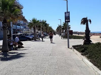 a man walking down a sidewalk with palm trees at Torre 6- Vista Cidade, Aconchegante, 80mt Praia, Wifi in Quarteira
