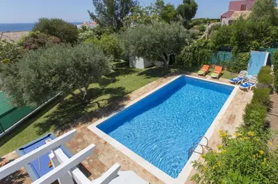 a swimming pool in a yard with chairs and trees at Villa Emilio Pequena by Villa Plus in Albufeira