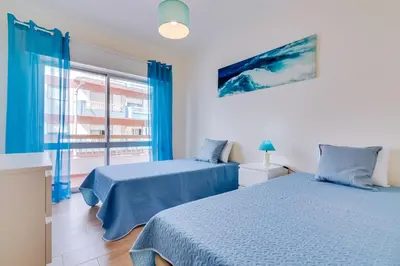 two beds in a room with blue curtains and a window at Quarteira 2Br - near the beach at Homesbyfc in Quarteira