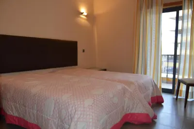 a bedroom with a bed and a large window at Apartamento frente ao mar com piscina de água salgada in Quarteira