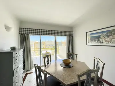 a dining room with a table and chairs and a balcony at Alcharb - Pool & City Center - Vilamoura in Quarteira