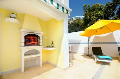 a patio with an outdoor fireplace and an umbrella at Villa Cubos by Villa Plus in Albufeira