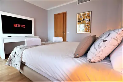 a bedroom with a large white bed with a flat screen tv at House J São Rafael - By Bedzy in Albufeira