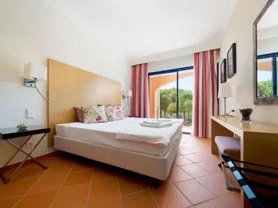 a bedroom with a bed and a desk and windows at AL - Apartamento Vila Sol F5 D in Vilamoura