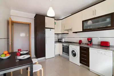 a kitchen with white cabinets and a table with a bowl of fruit at Apartamento Água Brisa in Albufeira