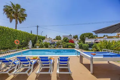 a swimming pool with chairs and a ping pong table at Villa Eliza by Villa Plus in Albufeira