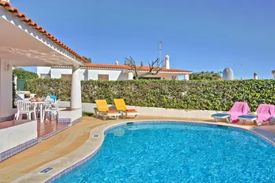 a swimming pool with chairs and a table and a house at Villa Vitor by Villa Plus in Albufeira