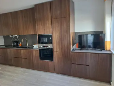 a kitchen with wooden cabinets and a flat screen tv at Quarteira 1-Bed Sleeps 4 Parking 1 min to Beach in Quarteira