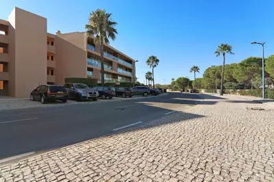 a street with parked cars and a building and palm trees at Salgados 4seasons Apartment in Albufeira