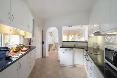 a large kitchen with white cabinets and black counter tops at Casa de Gales - Vilamoura in Vilamoura