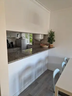 a kitchen with white walls and a counter with chairs at Apartamento T2 Palmeira Galé-Praia da Galé in Guia