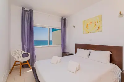 a bedroom with a bed and a window and a chair at Frente praia SIM T3 Praia Quarteira by HsRentals in Quarteira