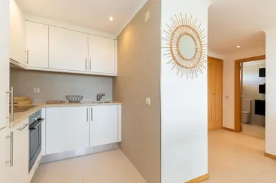 a kitchen with white cabinets and a mirror on the wall at Varandas do Castelo By Garvetur in Albufeira