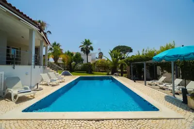 a swimming pool with chairs and an umbrella next to a house at Villa Sara in Quarteira