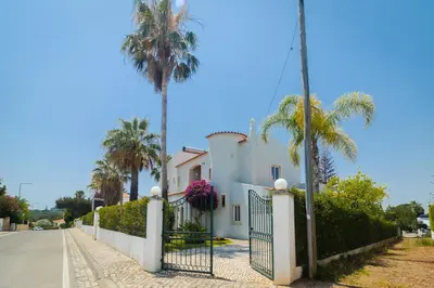 a white house with a fence and palm trees at Villa Sara in Quarteira