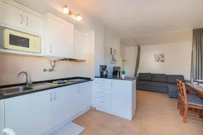 a kitchen with white cabinets and a living room with a couch at Vilamoura Cosy 2 with Pool by Homing in Vilamoura