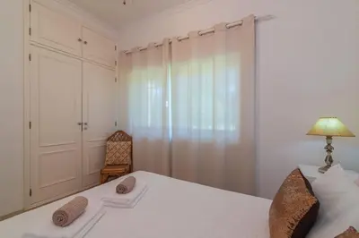 a white bedroom with a bed and a chair at Vilamoura - M M GARDEN - Magnifico T2 in Vilamoura