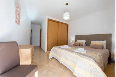 a bedroom with a large bed and a chair at Apartamento Monarquia - T3 Quarteira in Quarteira