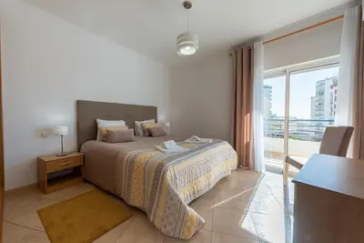 a bedroom with a bed and a large window at Apartamento Monarquia - T3 Quarteira in Quarteira