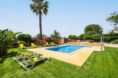 a swimming pool in a yard with chairs and a palm tree at Villa Bali by Algarve Vacation in Albufeira
