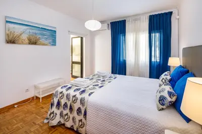a bedroom with a large bed with blue curtains at Apartamento Vista Mar T2 in Quarteira