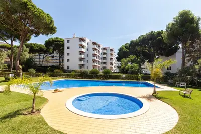 a swimming pool in a garden with a building in the background at Centralgarve - Great, Bright 2-bedroom Flat in the Center of Vilamoura -Topázio in Vilamoura