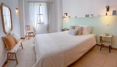 a bedroom with a large white bed and a chair at Apartamentos Ninho das Gaivotas in Albufeira