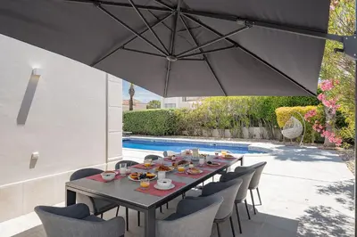 a wooden table with chairs and an umbrella next to a pool at Villa Flamingo - Quinta do Mar in Almancil