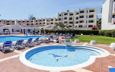 a swimming pool with chairs and a hotel in the background at Albufeira Garden in Albufeira
