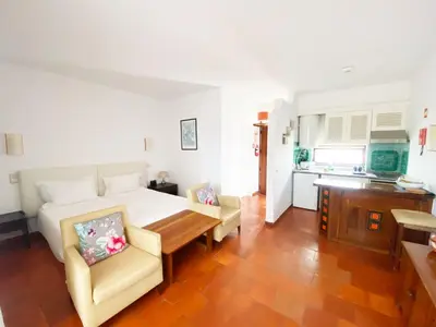 a bedroom with a bed and two chairs and a kitchen at Albufeira Garden in Albufeira