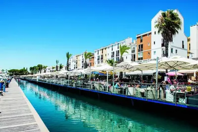 a canal with tables and umbrellas next to a city at VilamouraSun Aquamar 406 - Vista Marina in Quarteira