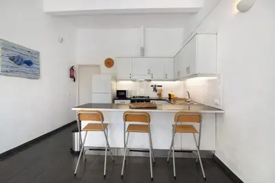 a kitchen with white cabinets and a counter with three chairs at Vila Rafa in Albufeira