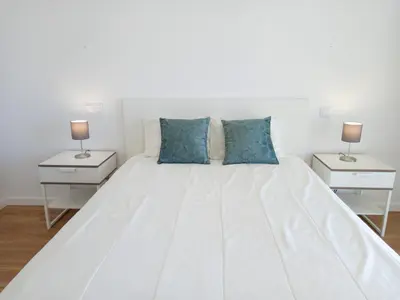 a white bed with blue pillows in a bedroom at T3 Alto Forte -Vista Mar,Ar Condicionado,Garagem in Quarteira