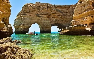 a boat in the ocean with an arch in the water at ALDEIA DAS AÇOTEIAS VILLAGEs in Albufeira