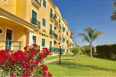 a large yellow building with red flowers in a yard at São João das Areias By Albufeira Rental in Albufeira