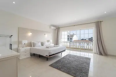 a white bedroom with a bed and a large window at Villa Lemos by HelloVacations in Albufeira