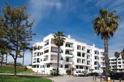a white apartment building with palm trees in a parking lot at Tatiana 1 bedroom apartment in Albufeira