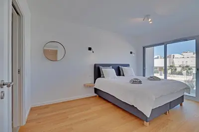 a white bedroom with a bed and a large window at Apartamento Vista Jardim by Portucasa in Albufeira