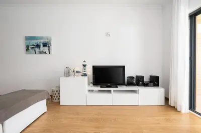 a white bedroom with a television on a white cabinet at Apartamento Janelas Oceano - Vilamoura in Quarteira