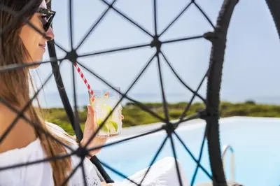 a woman holding a drink through a fence at Vila Maria Hotel - Adults Only in Albufeira