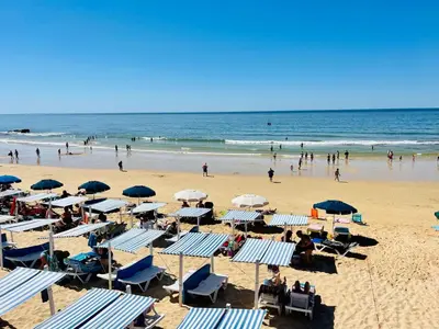 a beach with chairs and umbrellas and people in the ocean at On The BEACH Stunning Apartment Albufeira Olhos de Água in Albufeira