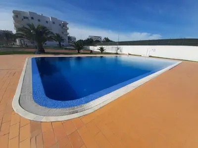 a blue swimming pool with a tile floor and a building at Apartamento Manelito House by Sunyway in Albufeira