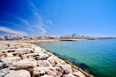 a beach with rocks and people on the water at Bright Modern Beachside Apartment with Pool & Seaview in Quarteira