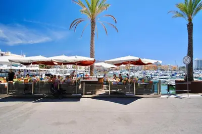 a group of people sitting under umbrellas near a marina at Bright Modern Beachside Apartment with Pool & Seaview in Quarteira
