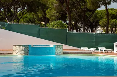 a swimming pool with blue water and a green fence at Açoteias B3 in Albufeira