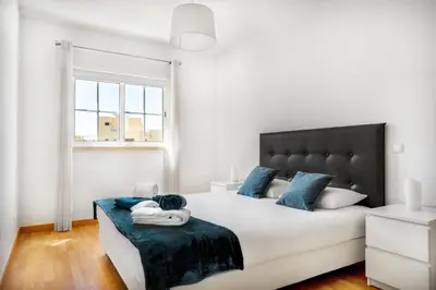 a white bedroom with a large bed with blue pillows at Apartamento no Condomínio Baia Village com Piscina in Albufeira